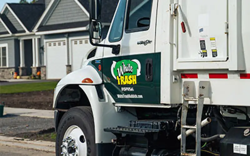 White Trash Disposal garbage truck parked on a suburban street in front of houses.