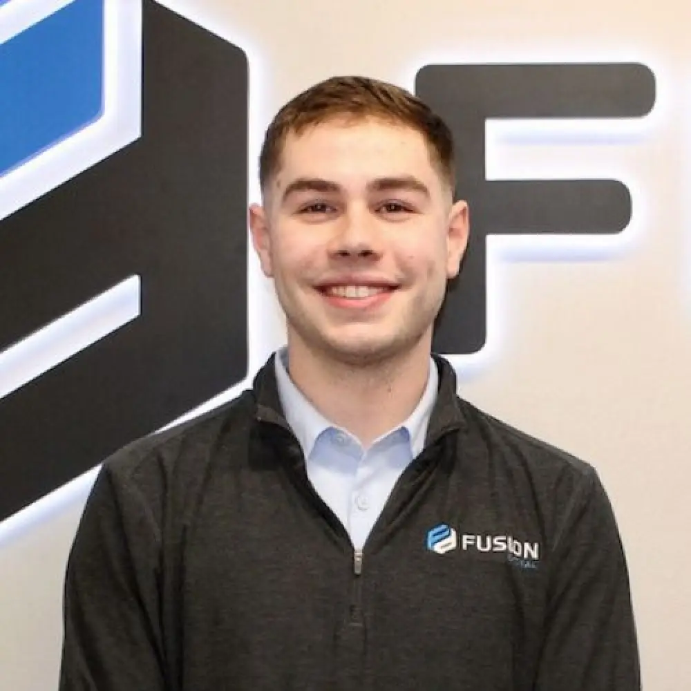 Young man smiling in front of a Fusion Digital logo, wearing a dark jacket with company branding.
