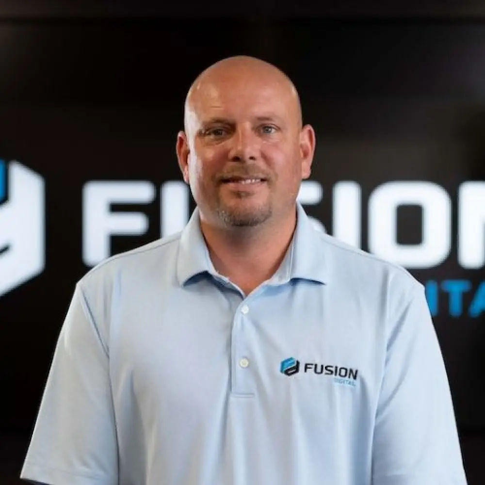 Bald man in a light blue Fusion Digital shirt standing in front of a Fusion Digital logo.