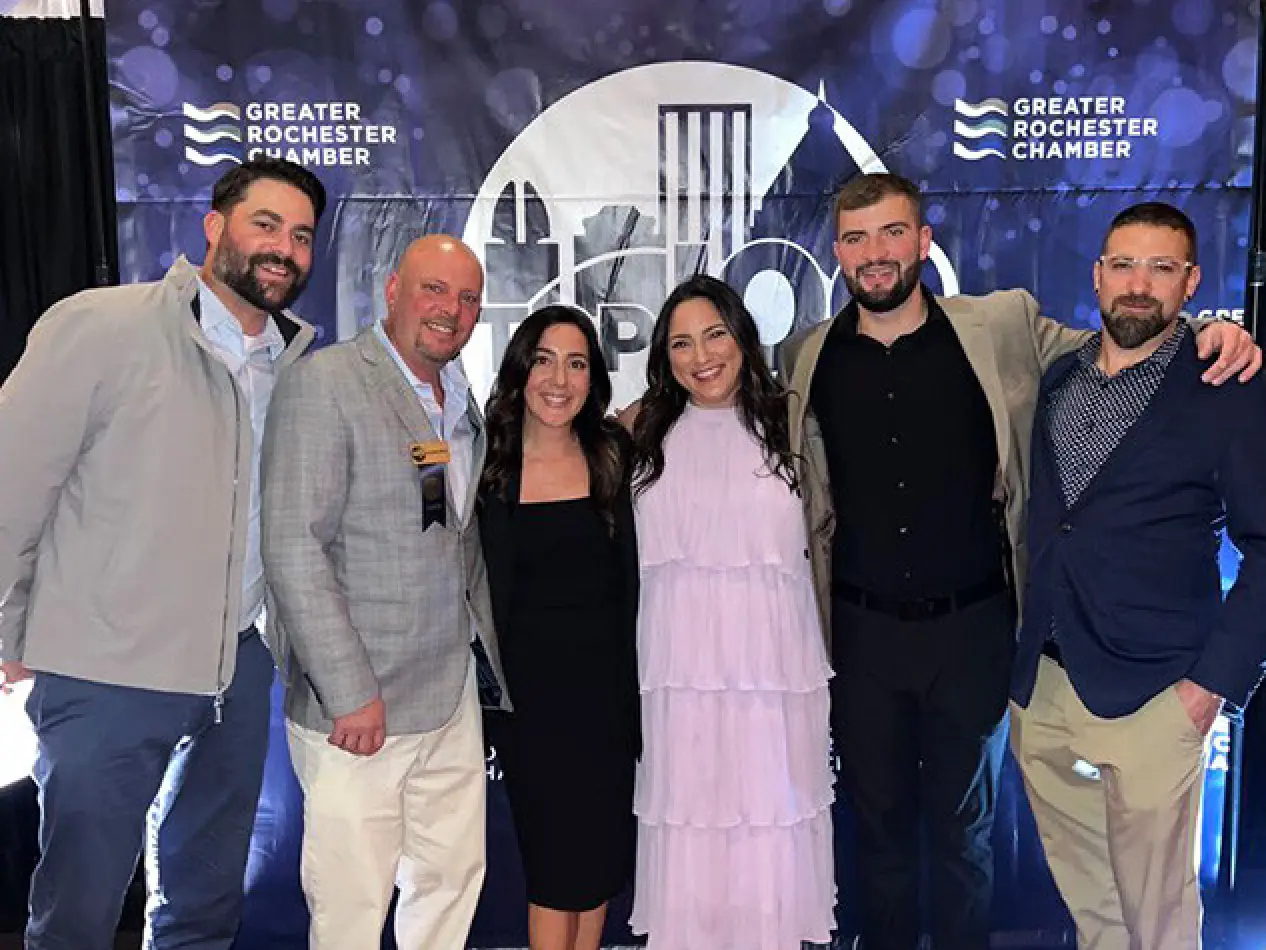 Six people smiling together in front of a Greater Rochester Chamber step-and-repeat banner.