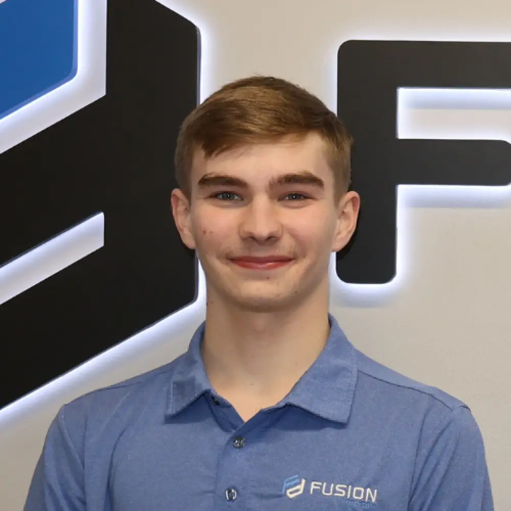 Smiling young person in a blue Fusion-branded shirt stands in front of a logo wall.