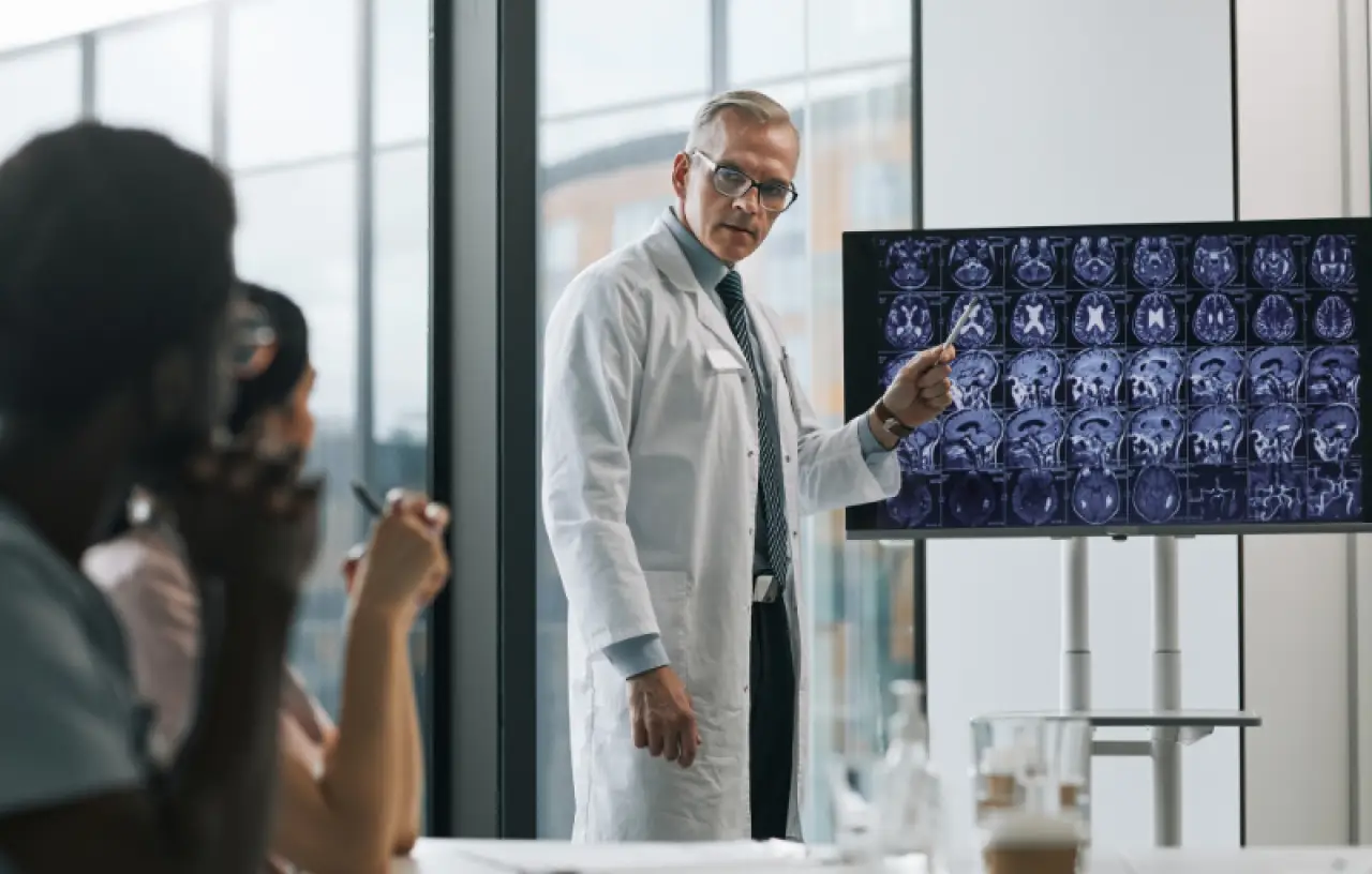 A doctor in a lab coat presents brain scan images to a group in a conference room.