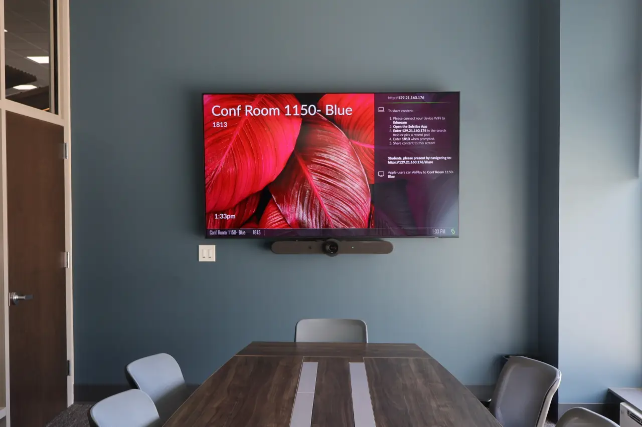 A conference room with a wall-mounted screen displaying a meeting schedule and red leaves.
