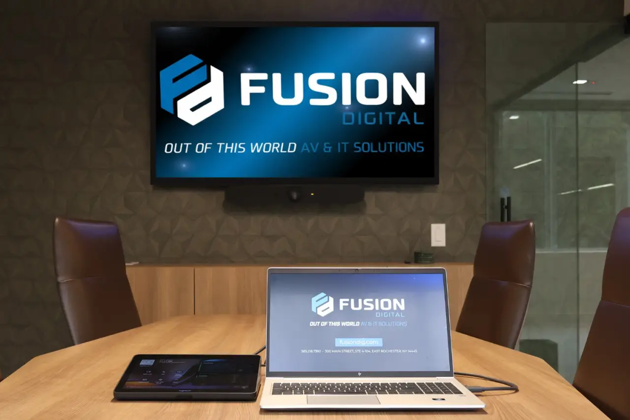 A conference room with a laptop and screen displaying FUSION DIGITAL AV IT SOLUTIONS branding.