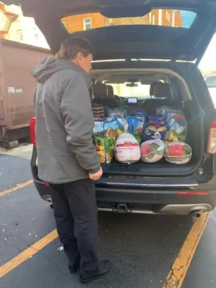 Person standing by an open car trunk filled with bags of groceries and frozen turkeys.