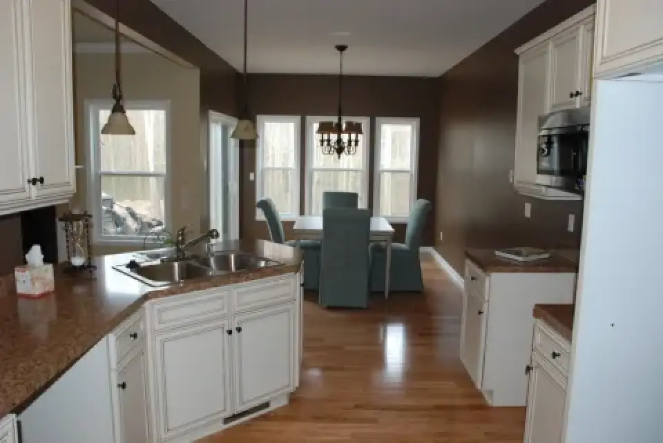 Modern kitchen with white cabinets, brown countertops, and dining area with blue chairs.
