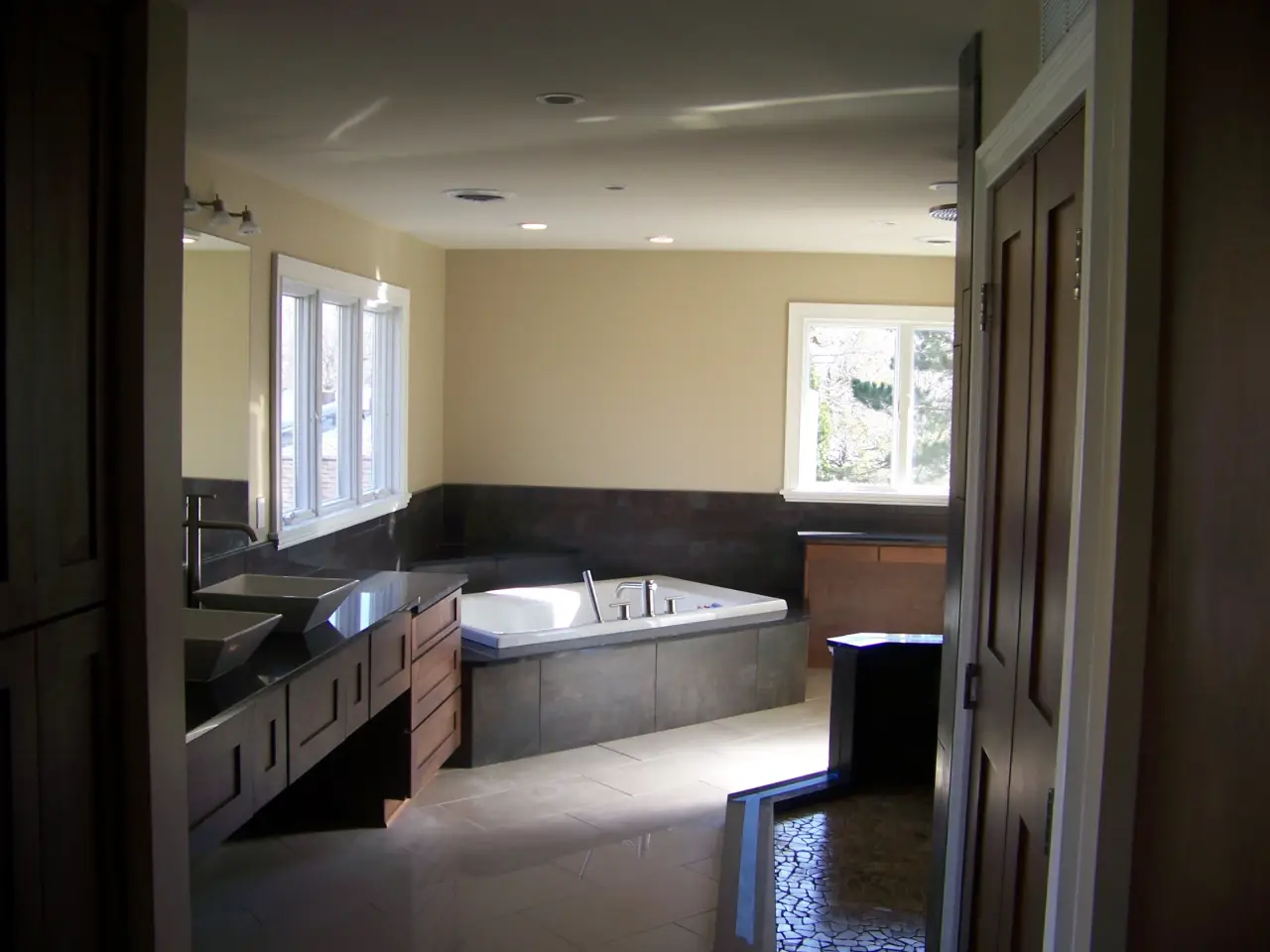 A spacious, modern bathroom featuring a jacuzzi, dual sinks, and large windows for natural light.