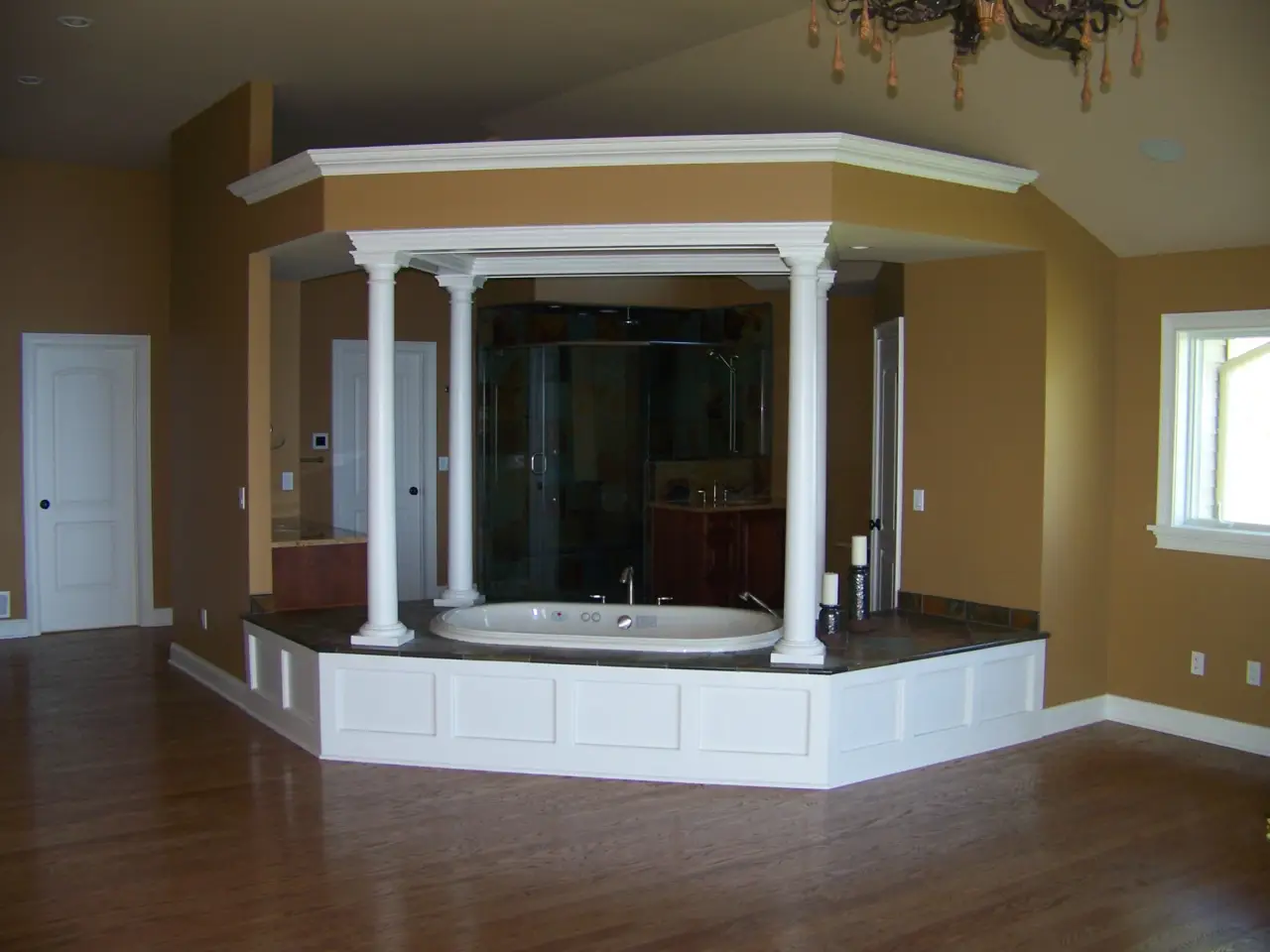 A spacious bathroom featuring a sunken tub surrounded by white columns, with a glass shower enclosure and warm brown walls.