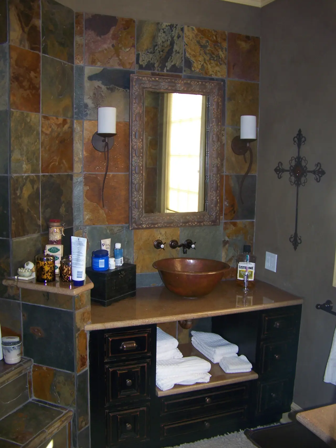 A stylish bathroom featuring a slate-tiled wall, a copper sink, a framed mirror, and neatly arranged towels.