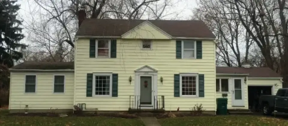 Light yellow two-story house with green shutters, a central door, and bare trees in the yard.