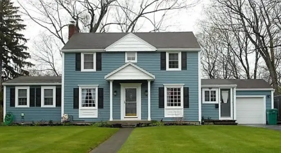 Two-story blue house with white trim, black shutters, and attached garage on a grassy lawn.