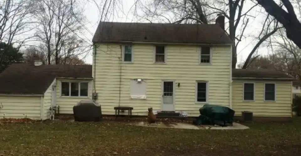 Two-story yellow house with side additions, bare trees, and covered items in a backyard.