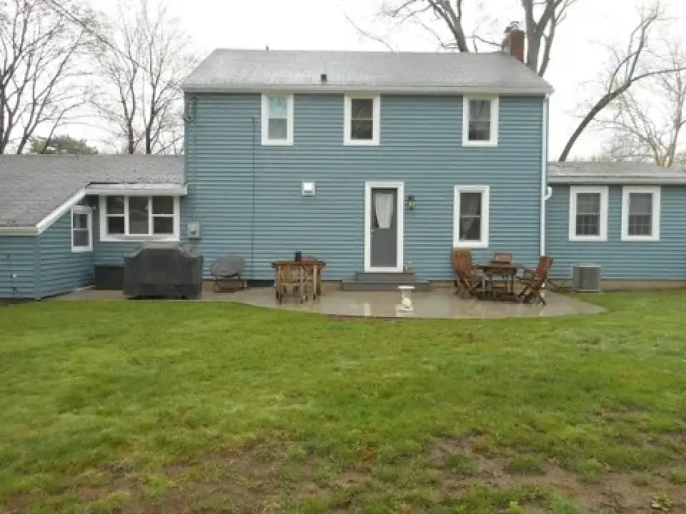 Blue two-story house with patio furniture on a concrete patio and green grass in the backyard.