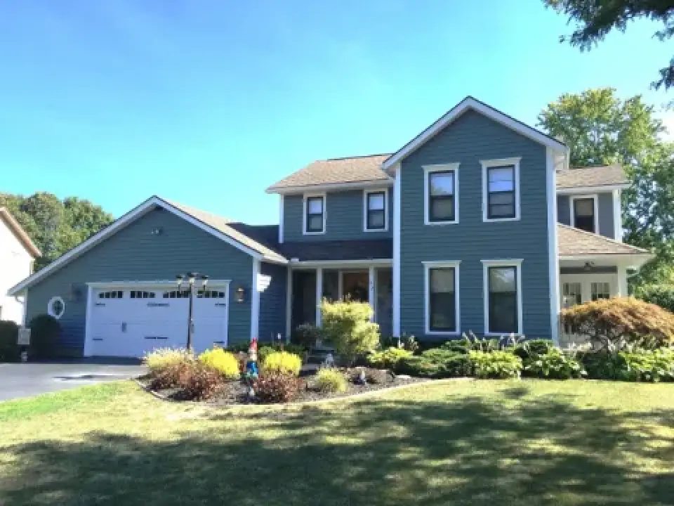 Blue two-story house with white trim, attached garage, garden, and sunny front yard.