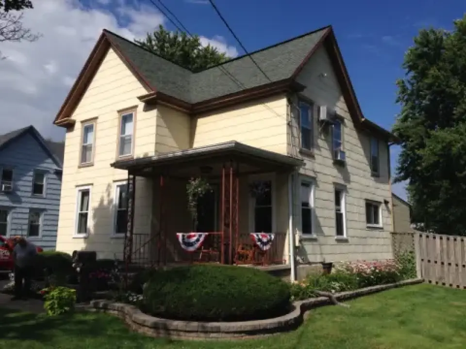 A two-story yellow house with a front porch, decorated with patriotic red, white, and blue bunting.