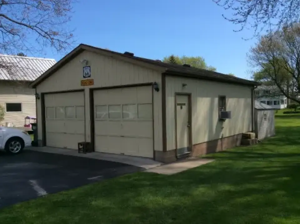 A beige two-car garage with closed doors, beside a driveway and surrounded by green grass.