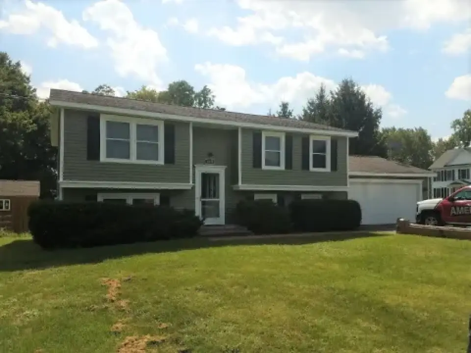 A split-level gray house with white trim, attached garage, front lawn, and bushes.