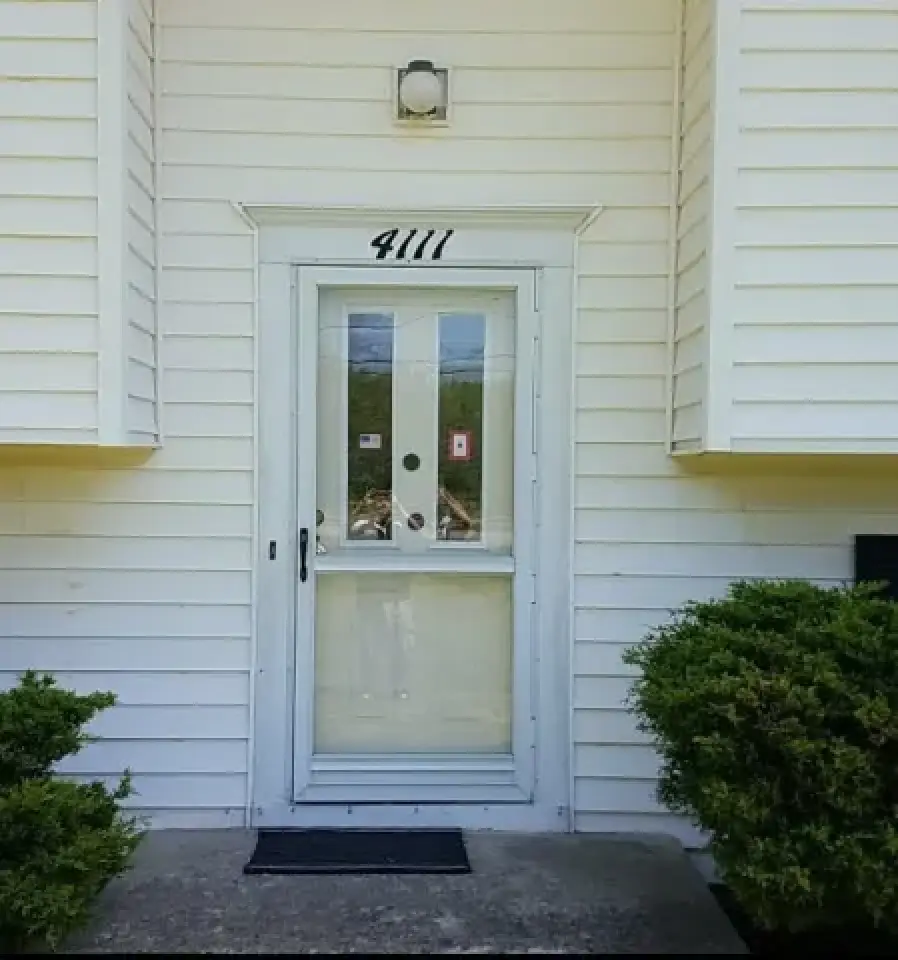 White front door with glass storm door, house number 4111 above, bushes on both sides.