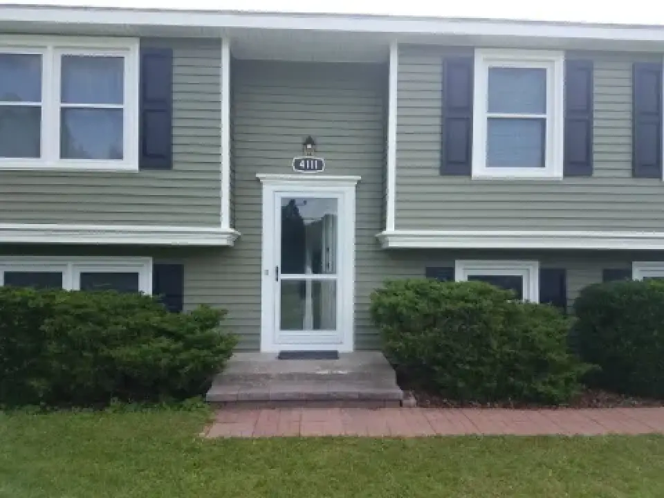 Split-level house with green siding, white trim, and shrubs in front of the entryway.