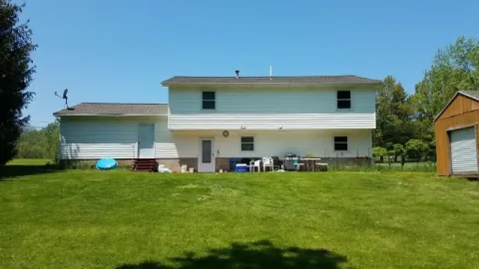 A two-story white house with a large green yard and a small shed under a clear blue sky.