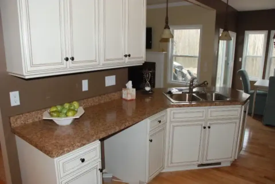 White kitchen cabinets with brown countertops, a bowl of green apples, and a double sink.