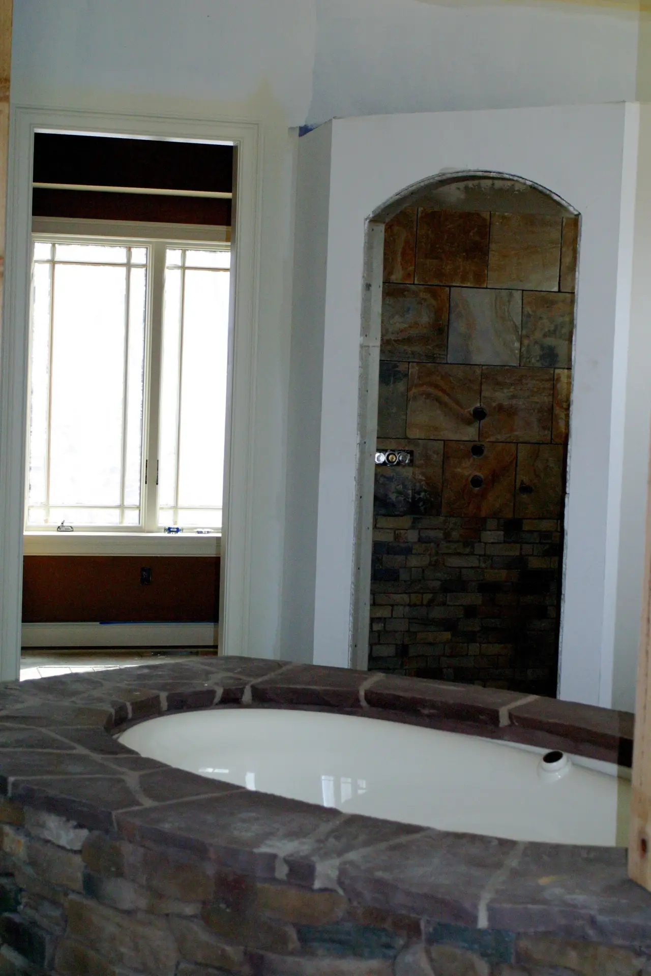 A bathroom under construction featuring a stone tub and a tiled shower area, with a window visible in the background.