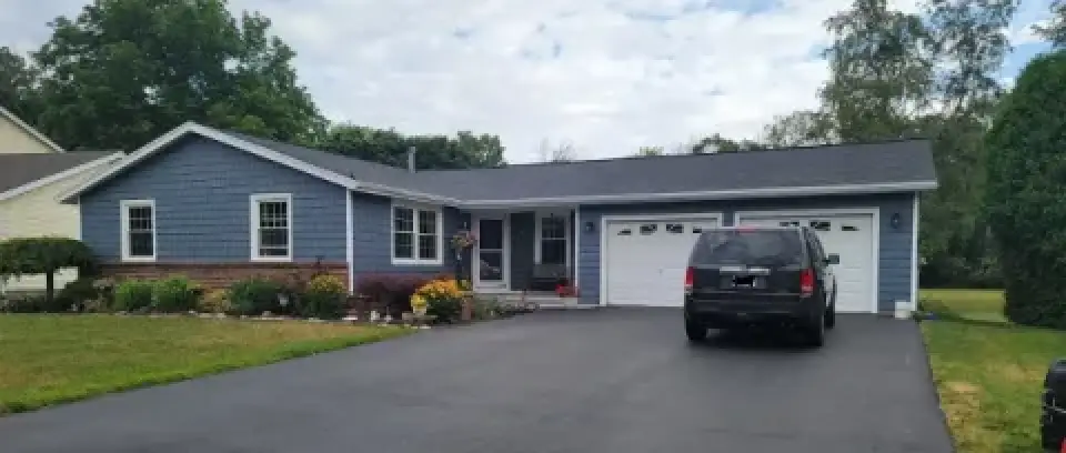 Single-story blue house with attached garage, black SUV parked in driveway, and landscaped yard.