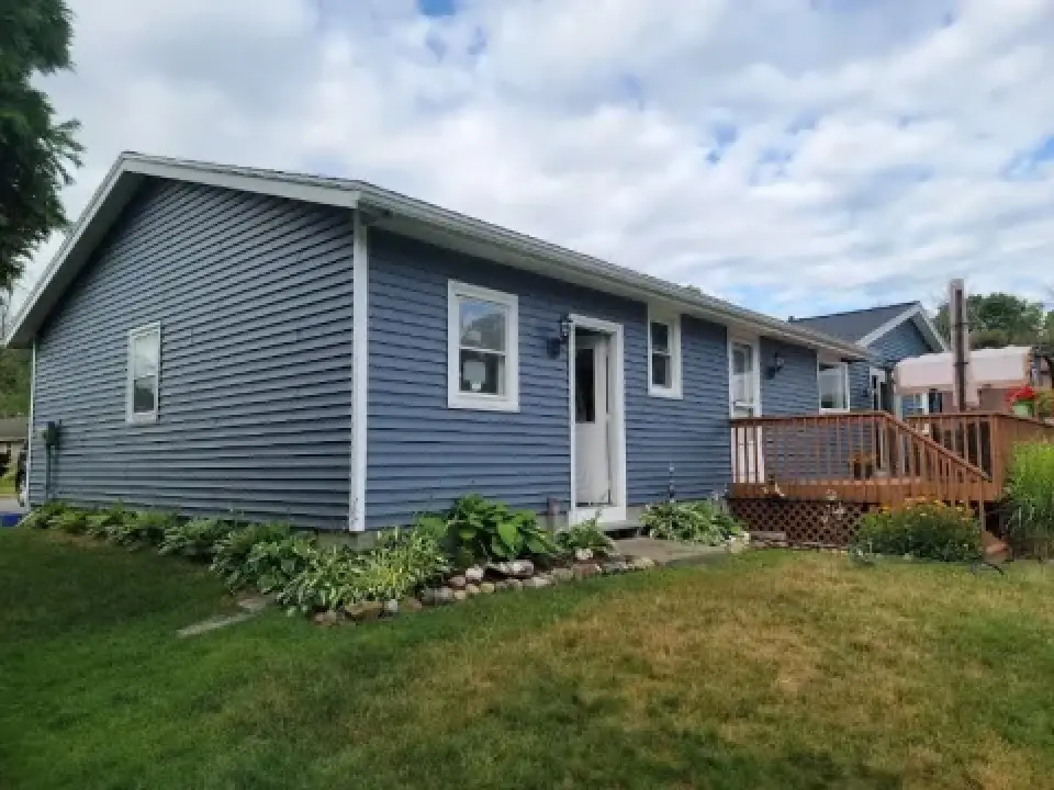 Blue single-story house with white trim, small porch, and a grassy yard under a cloudy sky.