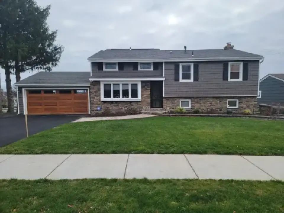 Gray split-level house with a two-car garage, stone facade, and a large green front lawn.