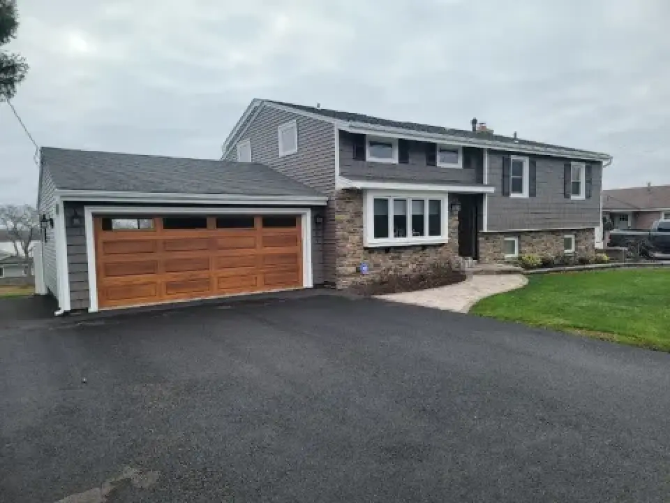 Gray split-level house with a stone facade and wooden garage door, newly paved driveway.