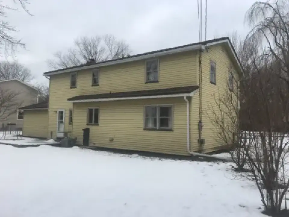 Two-story yellow house with snow-covered yard and overcast sky.