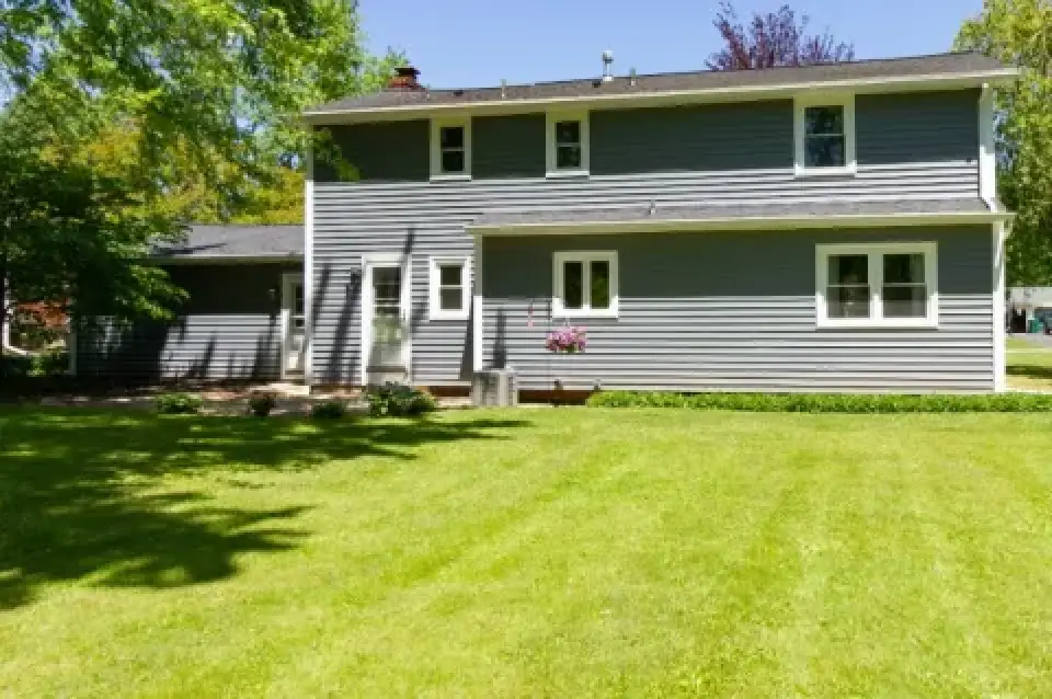 Gray two-story house with white trim and a large green lawn in sunny weather.