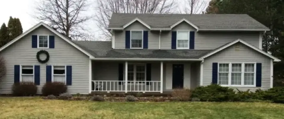 Gray two-story house with blue shutters, a front porch, and a wreath on the left side.