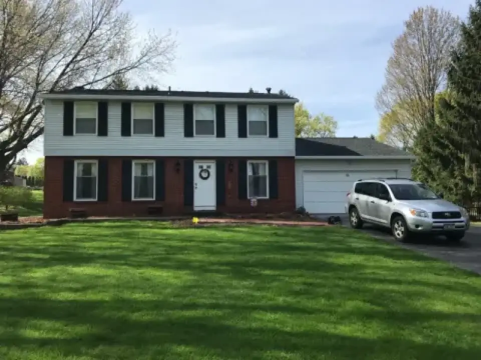 A two-story house with a car parked in the driveway and green grass in the front yard.