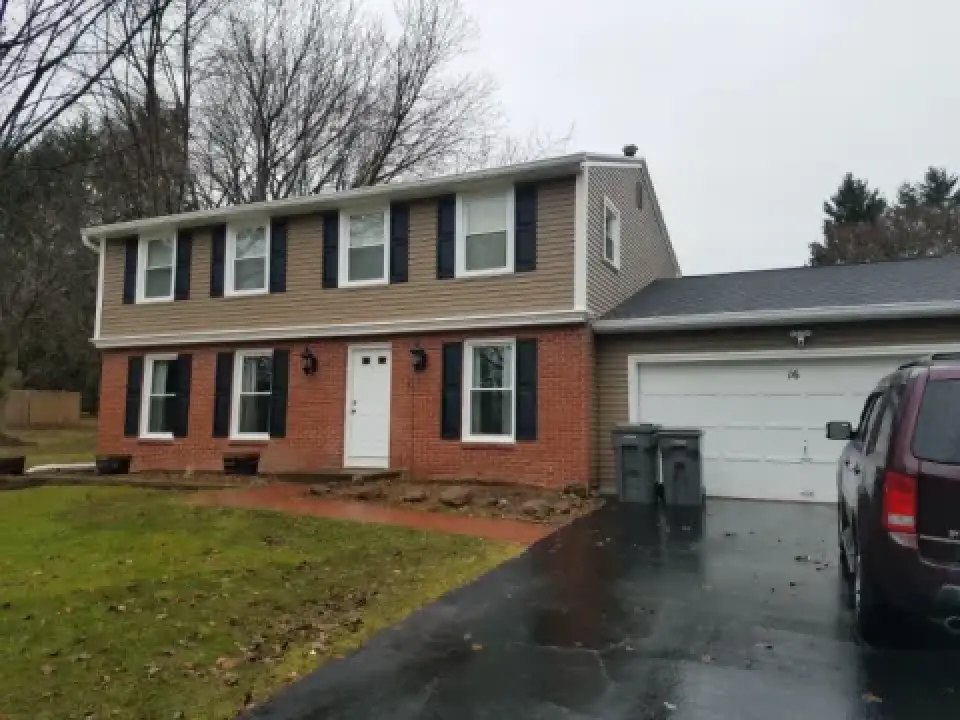 Two-story brick and siding house with black shutters, attached garage, and a car in driveway.