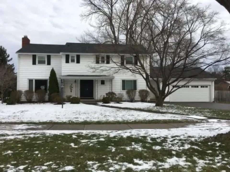 Two-story white house with black shutters, bare trees, and patchy snow on the lawn.