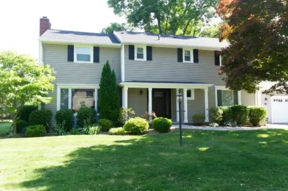 Two-story suburban house with beige siding, black shutters, and a well-kept front lawn.