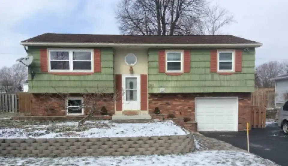 Green split-level house with red shutters, brick lower half, and light snow on the ground.