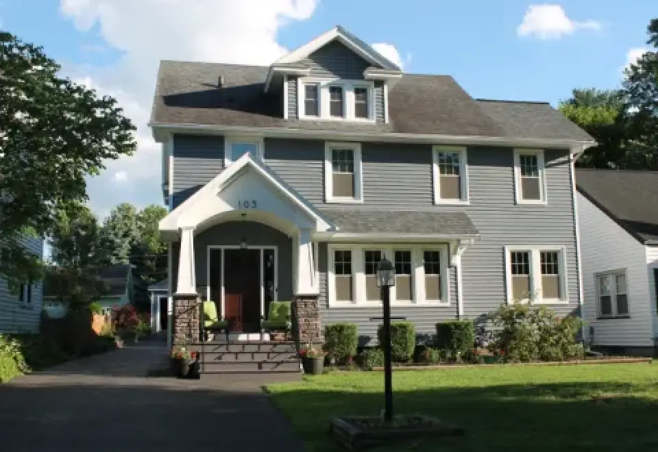 Two-story gray house with white trim, front porch, and green lawn under a blue sky.