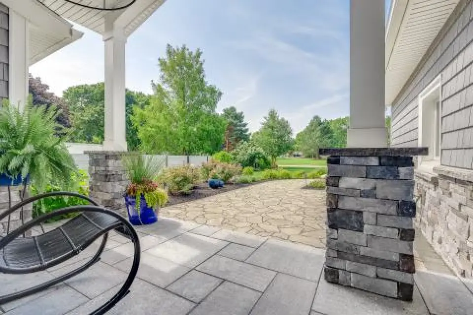 View from a porch with stone columns, patio, plants, and green trees in the background.