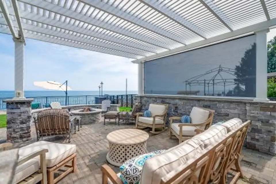 Outdoor patio with lounge seating, pergola overhead, and view of the ocean in the background.