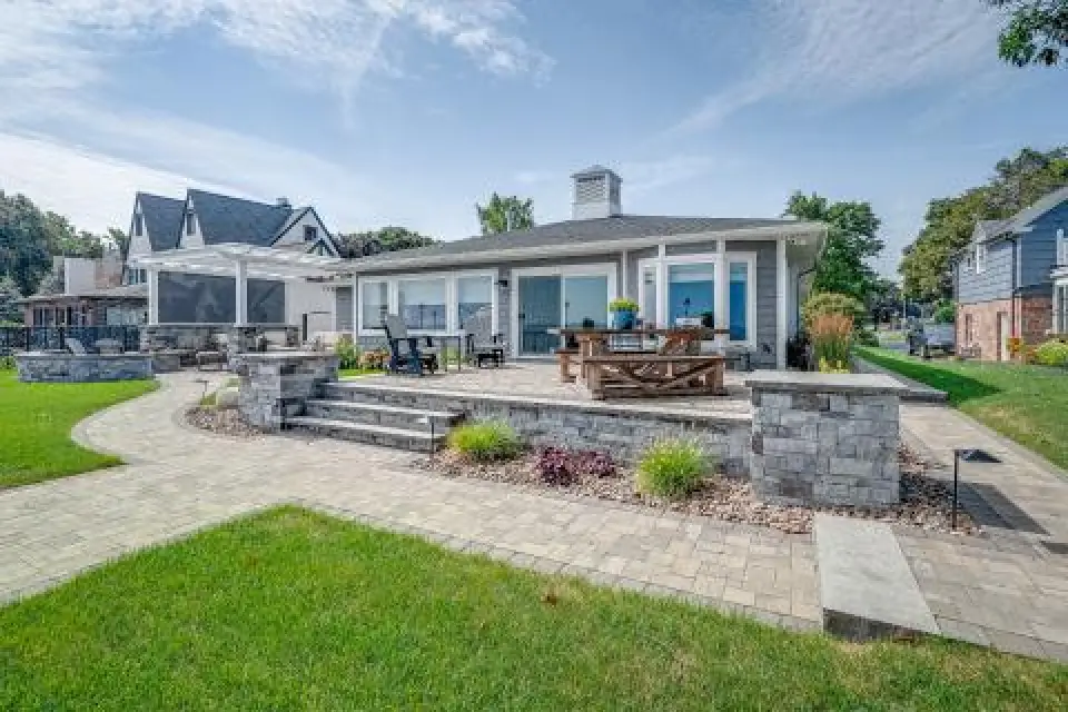 Modern house with large windows, patio seating, and a landscaped yard with stonework.