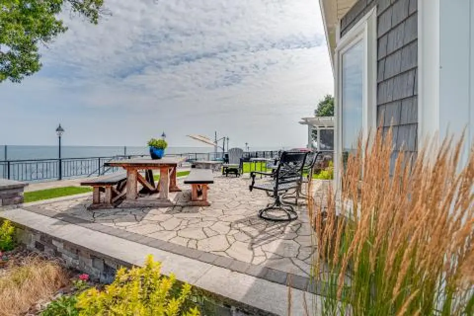 Patio with benches, a table, and lake view under a partly cloudy sky near a house.