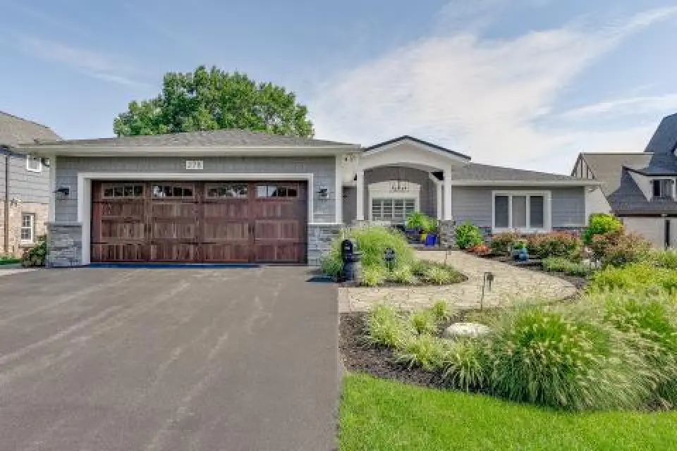 Single-story gray house with a wooden garage door and landscaped front yard on a sunny day.