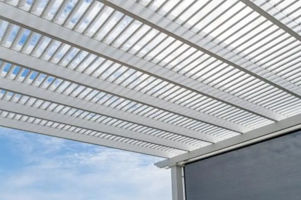 White louvered pergola roof with blue sky and clouds visible through the slats.