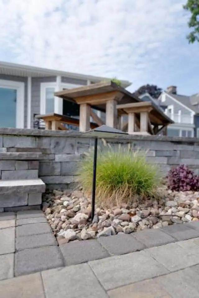 Outdoor patio with stone wall, picnic tables, greenery, and a landscape light fixture.