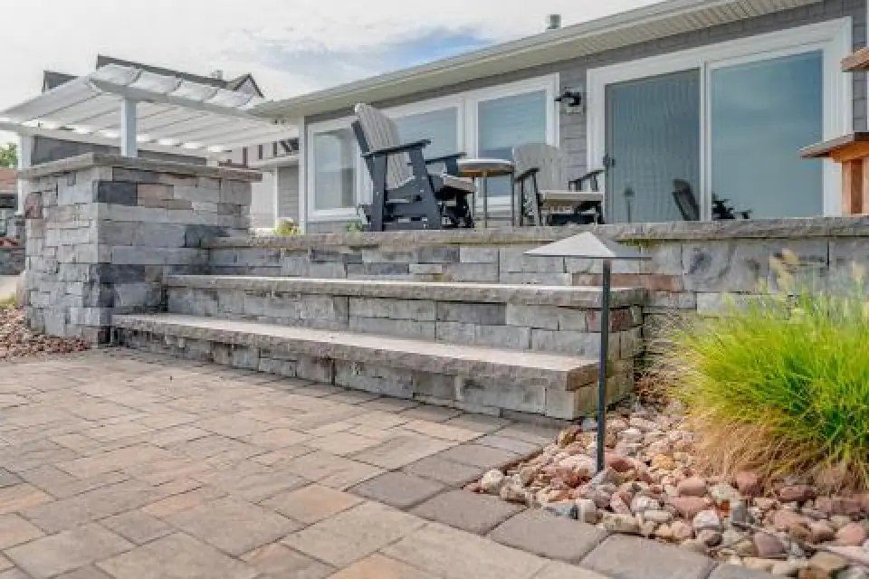 Stone patio steps with pavers, seating area, and decorative landscaping near a modern house.