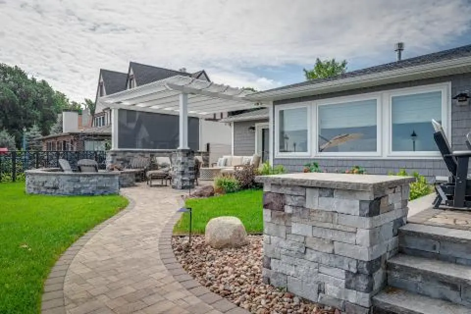 Backyard patio with a pergola, outdoor seating, stone path, and neatly landscaped garden.