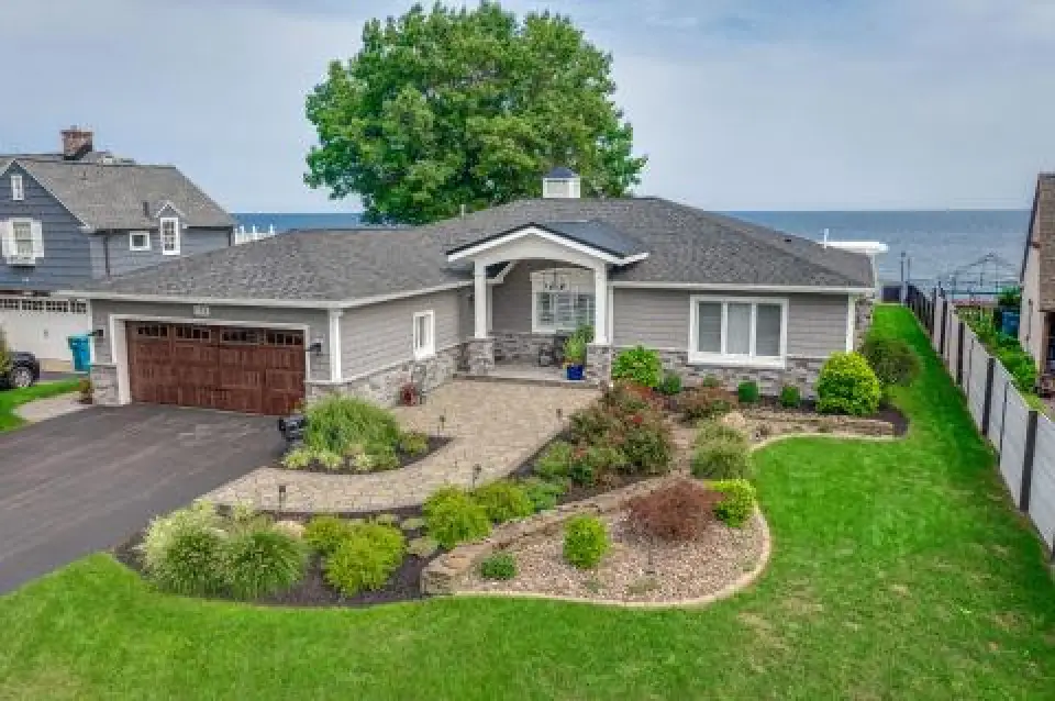 Single-story gray house with a landscaped yard, stone walkway, and view of the water behind.