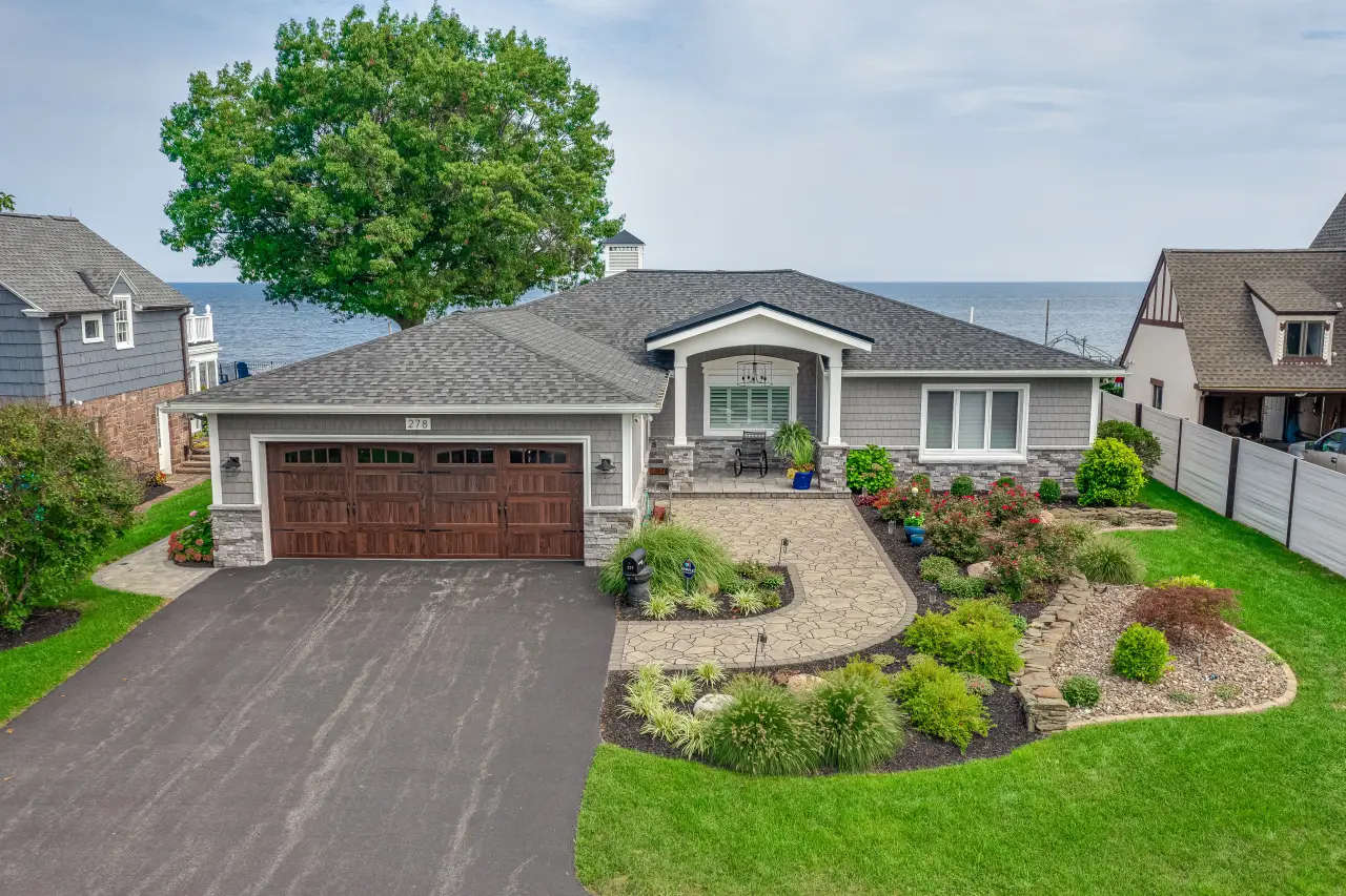Single-story gray house with a two-car garage and landscaped yard, overlooking a large body of water.